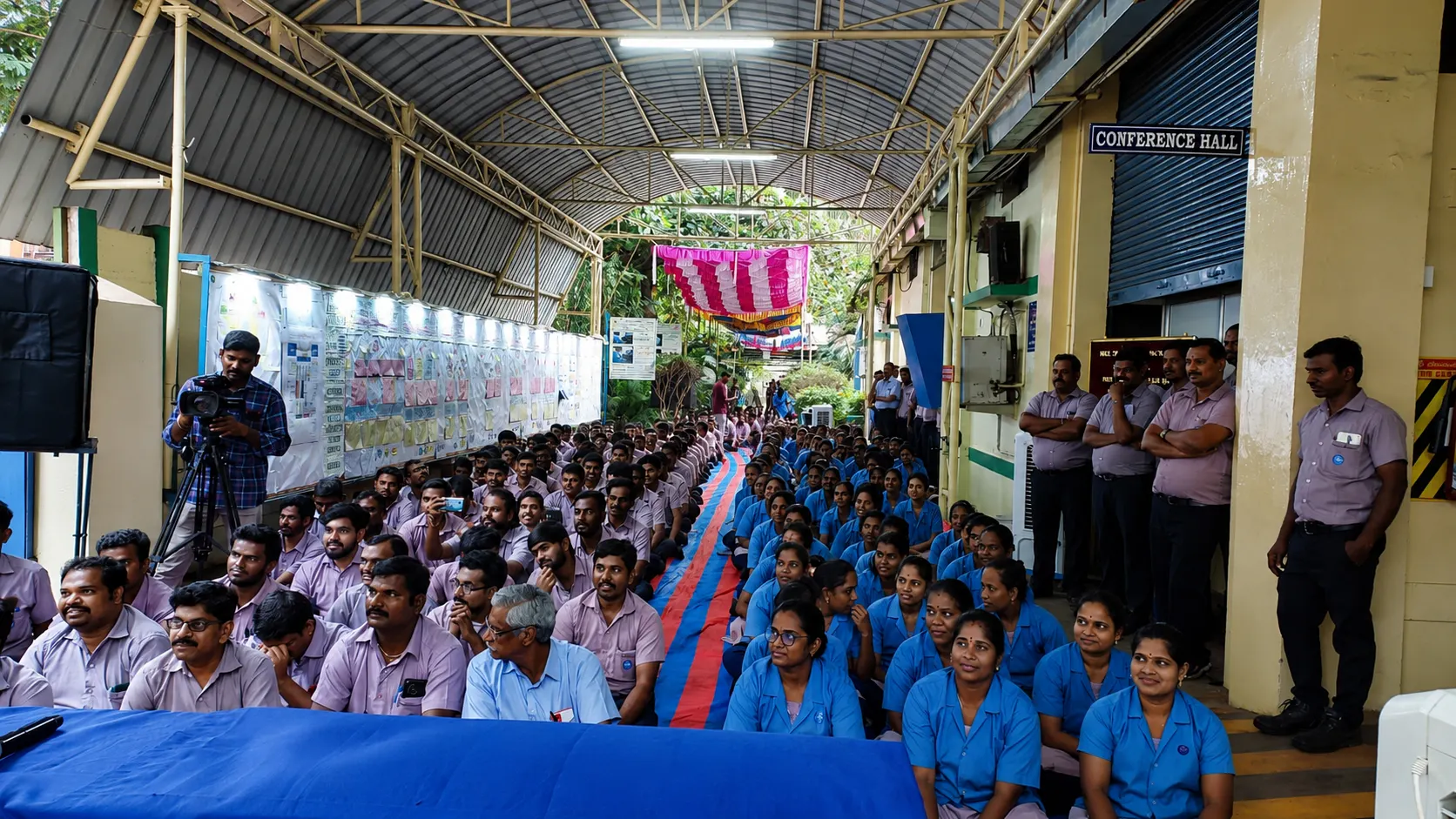 Large factory workforce seated for a briefing under a covered walkway